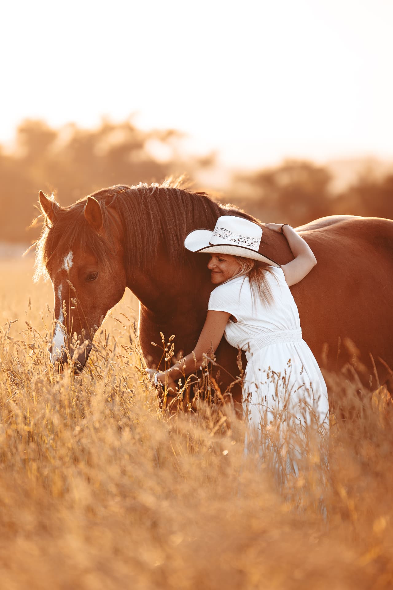 Femme enlaçant son cheval dans un champ doré au soleil couchant
