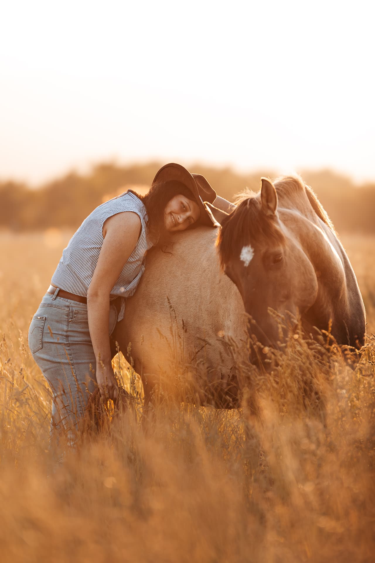 Fanny enlace un cheval dans un champ doré au coucher du soleil